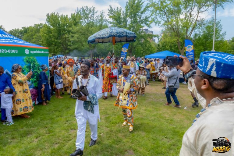 Festival Yemba Canada 2026 : cortège avançant sur la pelouse, musicien aux cloches doubles en tête